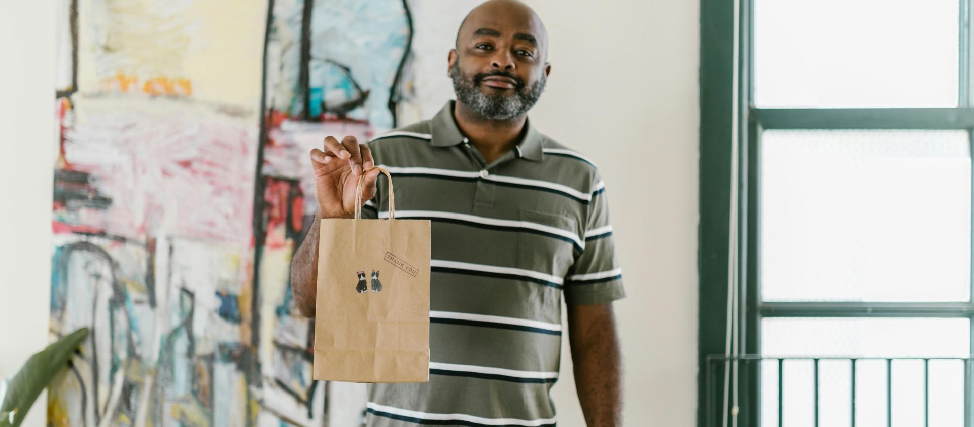 A smiling entrepreneur holding a paper bag with stickers in an artistic setting, showcasing small business creativity.