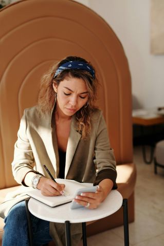 A woman jotting notes while using her smartphone in a stylish indoor setting.